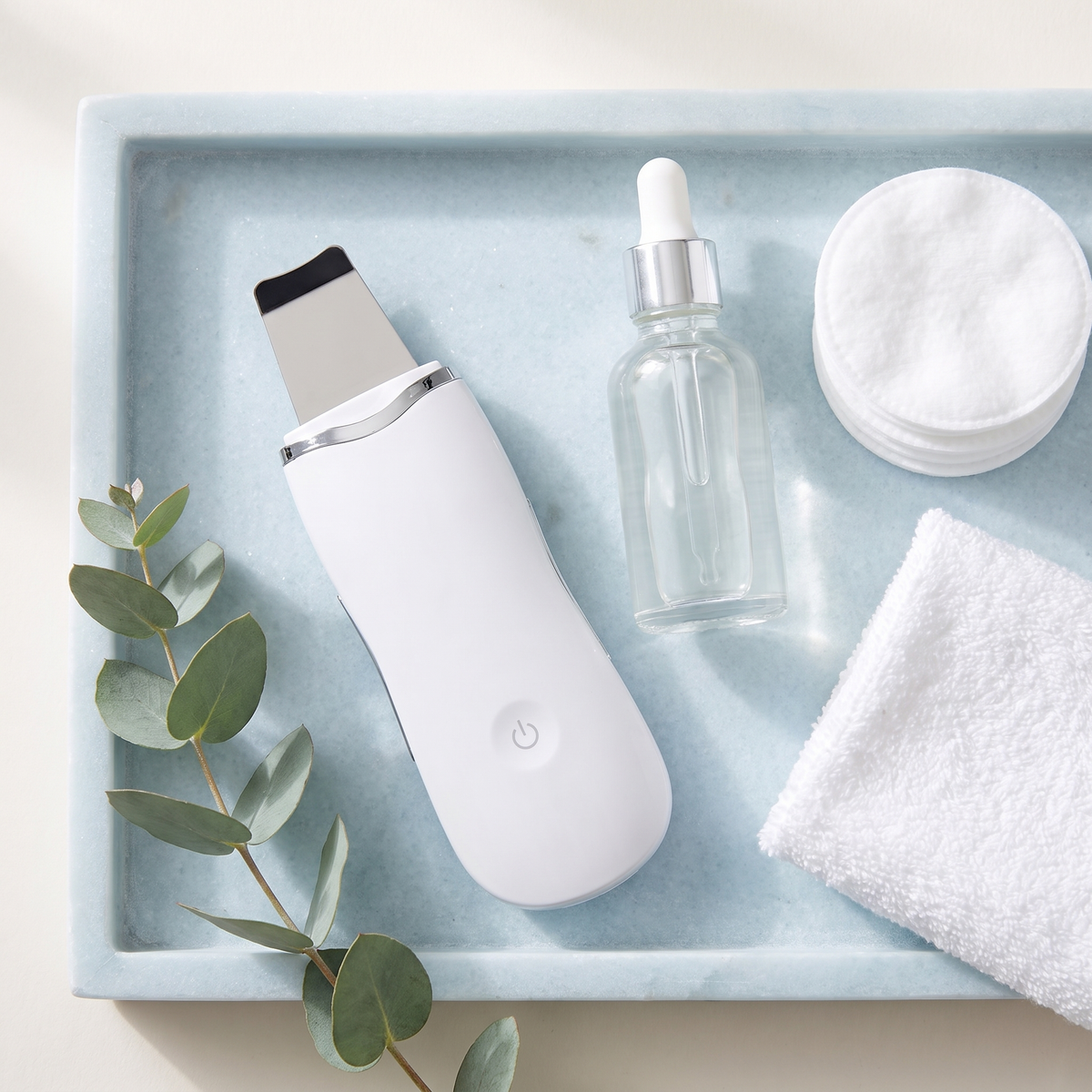Himra ultrasonic skin scrubber flat lay with serum and cotton pads