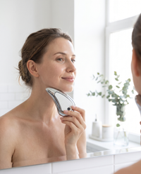Woman gliding the Himra heated gua sha along her jawline