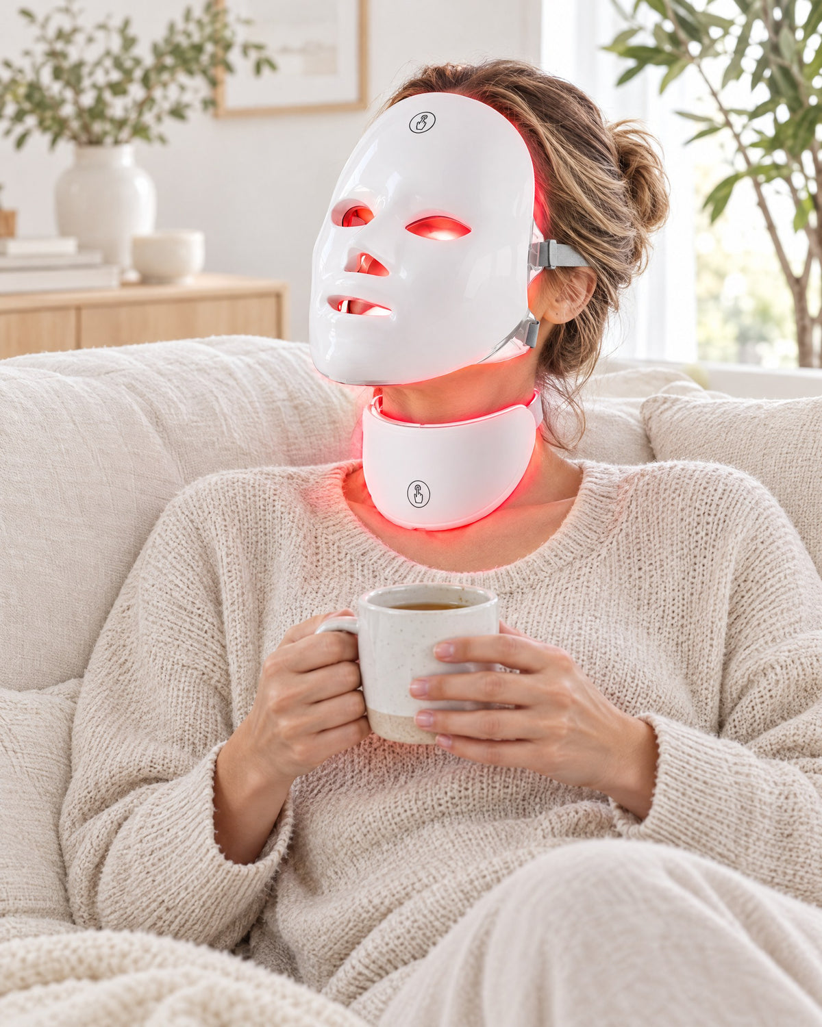 Woman relaxing on a sofa wearing the Himra LED face mask and neck piece in red light
