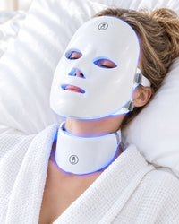 Woman lying in bed wearing the Himra LED face mask and neck piece in blue light